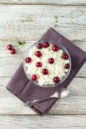 Breakfast from cottage cheese with cherry in transparent bowl on a white wooden backgroundの写真素材