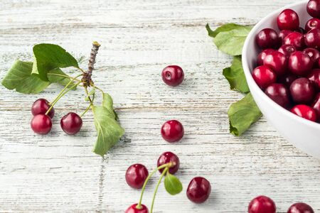 Fresh sweet cherries bowl with leaves in water drops on white wooden background, top view