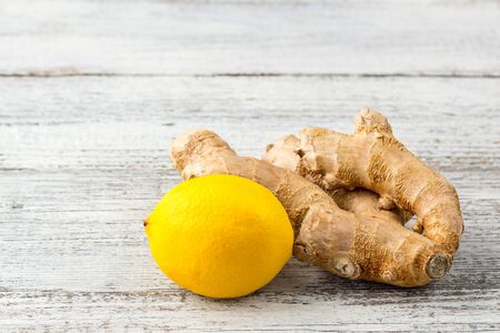 A piece of ginger and a yellow lemon on a white wooden background. Copy space