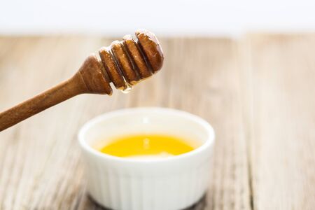 Honey in white bowl with wooden honey dipper on wooden table backgroundの写真素材