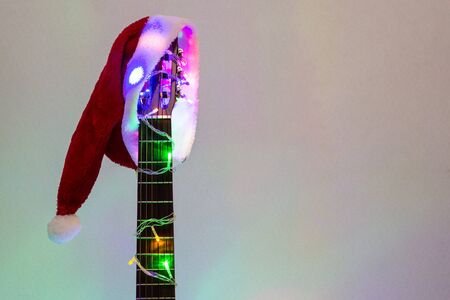 acoustic guitar with red Santa hat and light colorful garland. Christmas music concept on white backgroundの写真素材