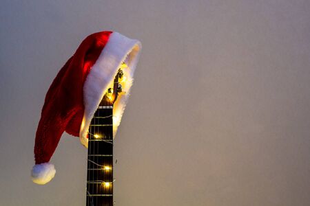 Acoustic Guitar with red Santa hat and light garland. Christmas music song concept with copyspace on white backgroundの写真素材