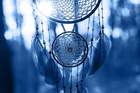 Dreamcatcher made of feathers leather beads and ropes in classic blue trendy color, hanging. background. Color of the year 2020の写真素材