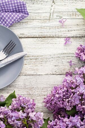 spring table setting with plate fork and knife decorated with lilac flowers on white wooden background. Top view with copy spaceの写真素材