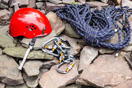 Rope access tools: hard hat, rope, carabiner. Mountaineering equipment on rocks against a background...