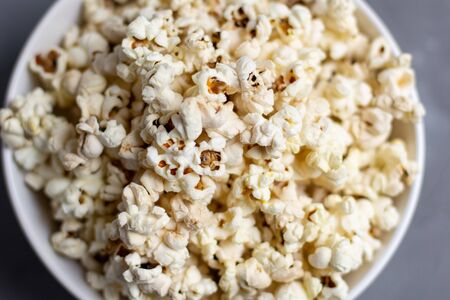 Popcorn in white bowl on grey table. Top view with copy space