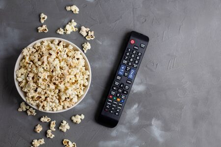 A white bowl of popcorn and TV remote on a grey background. The concept of watching TV, film, TV series, sports, shows.の写真素材