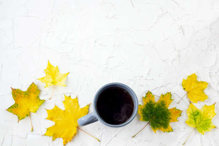 coffee in gray cup with autumn yellow maple leaves on white tableの写真素材