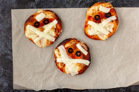 Mini pizza as mummy for kids with cheese, olives and ketchup. Funny crazy Halloween food for...