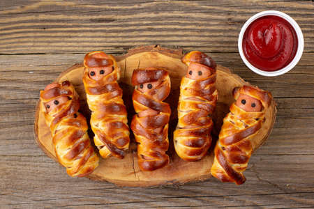 Scary sausage mummies in dough for kids party. Funny crazy Halloween food for children on wooden backgroundの写真素材