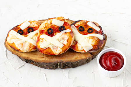 Mini pizza as mummy for kids with cheese, olives and ketchup. Funny crazy Halloween food for...