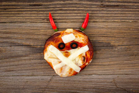 Mini pizza as mummy with horns for kids with cheese, olives and ketchup. Funny crazy Halloween food for children on wooden backgroundの写真素材