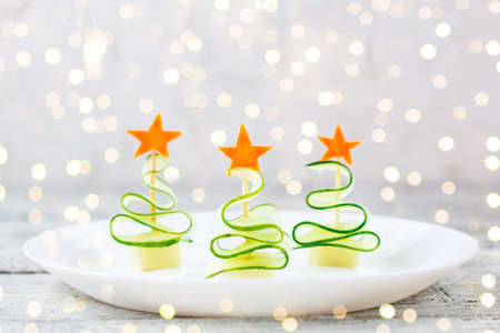 Creative concept set christmas trees of cucumber, cheese and star of carrot. Funny kids food for new year party on white plate with copy spaceの写真素材