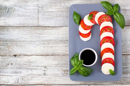 Christmas caprese salad in form of candy cane. Mozzarella and tomato on gray plate served for New year on white wooden backgroundの写真素材