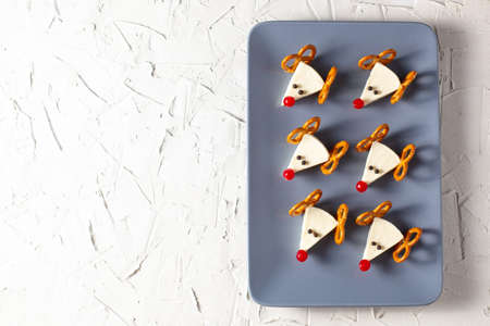 Funny christmas snack in a shapes of deer for kids party. Concept New year food from cheese and pretzels on white backgroundの写真素材