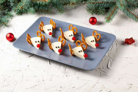 Funny christmas snack in a shapes of deer for kids party. Concept New year food from cheese and pretzels on white backgroundの写真素材