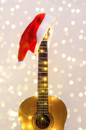 Acoustic Guitar with red Santa hat and light garland with bokeh. Christmas music song concept with copyspace on white backgroundの写真素材