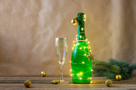 a bottle of green champagne wrapped in a glowing garland like a Christmas tree and glass. New year concept on natural backgroundの写真素材