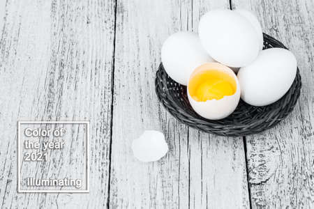 Broke One whole egg amongst white eggs in basket on a white wooden background. Color of the year 2021の写真素材