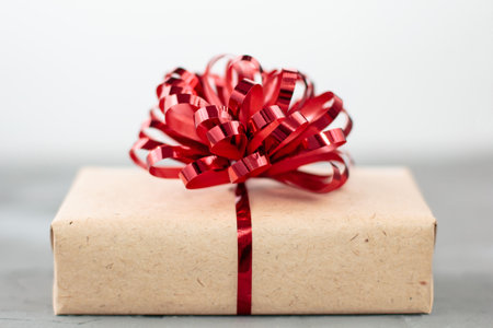 present box in craft paper with red bow on gray background