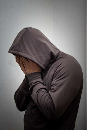 portrait of young adult man in the gray hood covered his face with his hands. The concept of addiction and alcoholism, depression and hopelessnessの写真素材