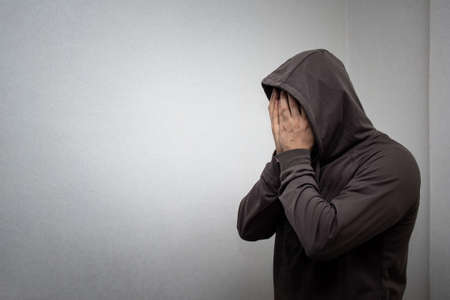 portrait of young adult man in the gray hood covered his face with his hands. The concept of addiction and alcoholism, depression and hopelessnessの写真素材
