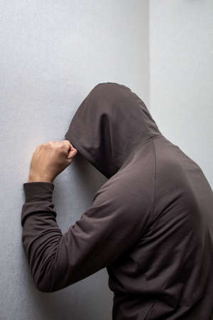 angry man in a gray hood slams his fist against the white wallの写真素材