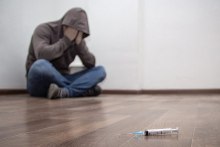 Syringe and man drug addict without of focus sitting in corner in the background. With copy spaceの写真素材