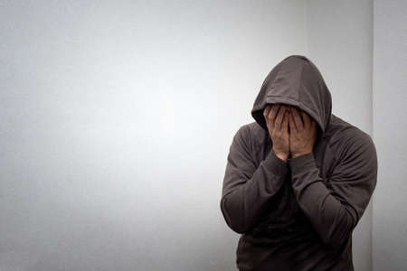 portrait of young adult man in the gray hood covered his face with his hands. The concept of...