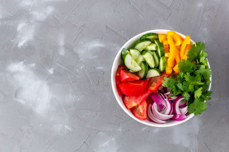 Plate of rainbow salad with different vegetables and herbs in white bowl on gray stone background. Top view with copyspaceの写真素材
