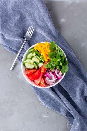 Plate of rainbow salad with different vegetables and herbs in white bowl with fork and napkin on gray stone background. Top viewの写真素材