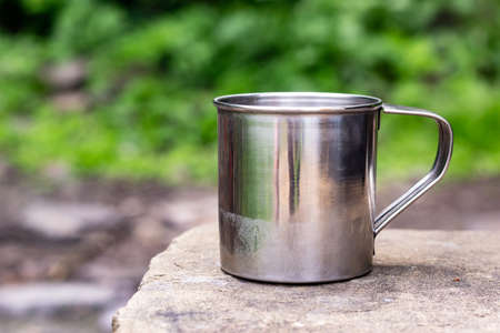 Stainless camping mug stands on the stones on front of natural green with copy spaceの写真素材