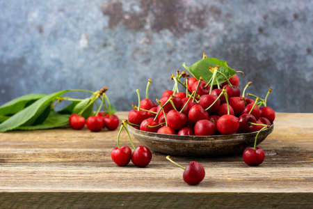 Ripe wet sweet cherries with green leaves in a metal plate on wooden backgroundの写真素材