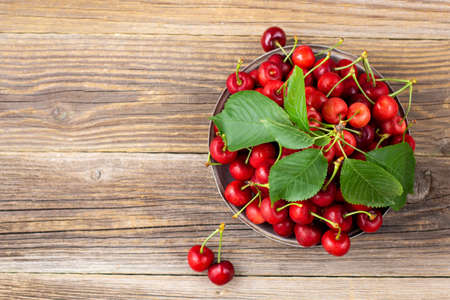 Ripe wet sweet cherries with green leaves in a metal plate on wooden background. Top view with...