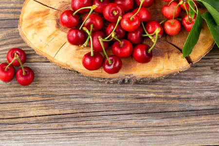 bunch of ripe sweet cherries with green leaves on wooden board. With copyspace