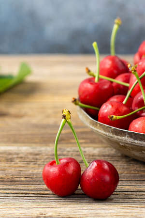 Ripe wet sweet cherries with green leaves in a metal plate on wooden backgroundの写真素材