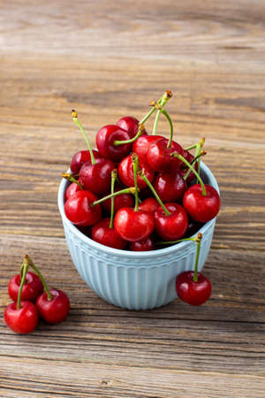 Ripe wet sweet cherries with drops in a blue bowl on wooden background with copyspaceの写真素材