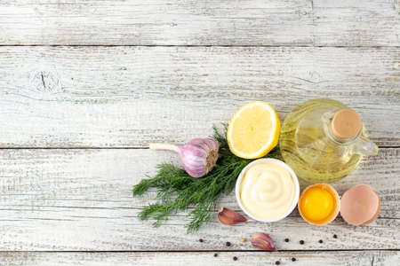 Mayonnaise sauce with garlic, egg, oil, lemon and herbs on white wooden background