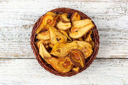 A pile of dried slices of pears in wicker basket on white wooden background. Dried fruit chips. Healthy food. Top viewの写真素材