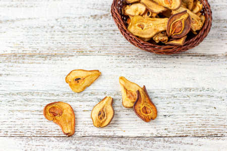 A pile of dried slices of pears in wicker basket on white wooden background. Dried fruit chips....