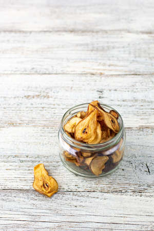 A pile of dried slices of pears in glass jar on white wooden background. Dried fruit chips. Healthy vegan foodの写真素材