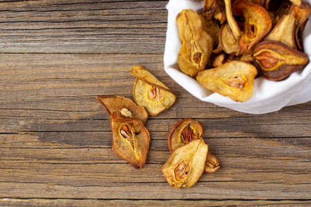 A pile of dried slices of pears in white pouch on wooden background. Dried fruit chips. Healthy vegan foodの写真素材