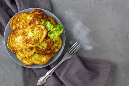 Fritters from zucchini in gray plate with sour cream sauce and greens. Vegetable pancakes of courgettes with green salad on gray background. Top view with copy spaceの写真素材