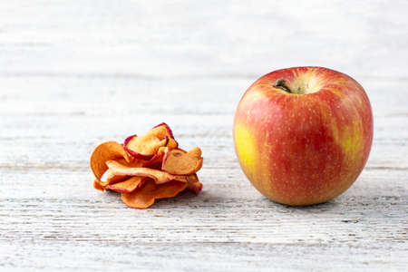 A pile of dried slices of apples and fresh ripe apples on wooden background. Dried fruit chips....