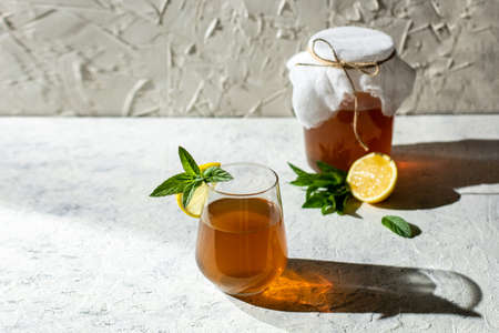 Raw fermented homemade alcoholic or non alcogolic kombucha superfood. Ice tea with healthy natural probiotic in glass with lemon slice and mint on white background. Hard shadowの写真素材