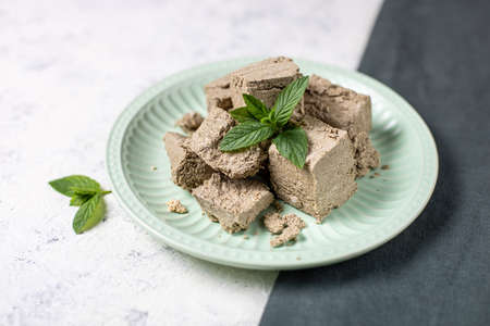 Pieces of halva on green plate. Sweet Turkish dessert with mint leaves on white backgroundの写真素材