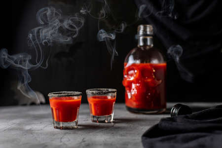Tomato cocktail in a skull-shaped bottle and glasses with smoke. Drink for Halloween party on dark...