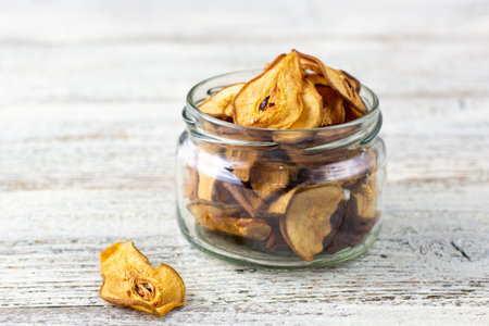 A pile of dried slices of pears in glass jar on white wooden background. Dried fruit chips. Healthy vegan foodの写真素材