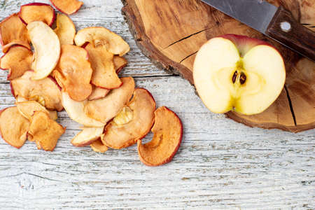 A pile of dried slices of apples and fresh ripe apples on wooden background. Dried fruit chips. Healthy vegan foodの写真素材