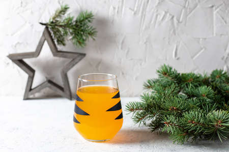 orange mandarin cocktail in glass with black stripes. Christmas holiday welcome drink. Concept for children new year with tree branchesの写真素材